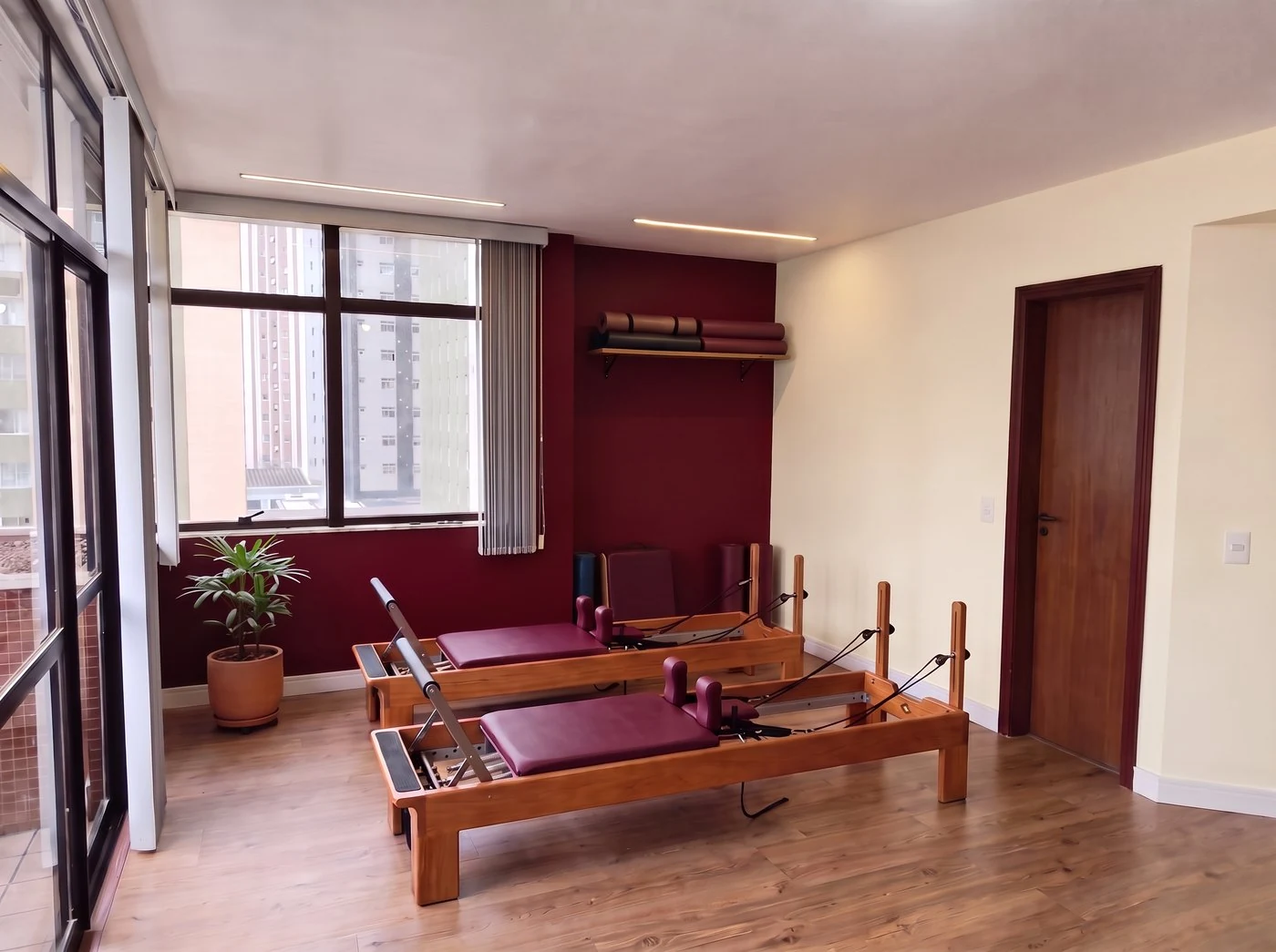 Sala de treino com dois Reformers de estofado bordô, parede bordô e janela ao fundo